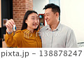A young Asian woman shares a smile with an older Asian man as they show off keys in a bright apartment. They appear happy and excited about their new place together. 138878247