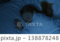 A girl with light brown hair sleeps peacefully under a white blanket. The room is dimly lit, creating a quiet and serene atmosphere. 138878248