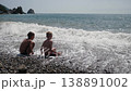 Two happy teenage boys are playing on the beach in stormy weather with big waves. Strong waves cover the two boys who are sitting on the shore. 138891002