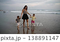 Mother running with her kids toward the ocean along a sandy beach at sunset 138891147