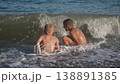 Two happy boys are playing on the beach with the waves. During summer holidays, children play with sea waves. The view from the back is beautiful. 138891385
