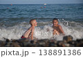 Two happy boys are playing on the beach with the waves. During summer holidays, children play with sea waves. The view from the back is beautiful. 138891386