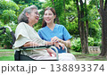 Caucasian woman caregiver encouraging senior patient on wheelchair in garden. 138893374
