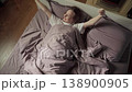 Happy young woman waking up in a comfortable cozy bed, stretching her arms and smiling as she greets the new day in her sunlit bedroom. High angle view capturing a moment of blissful awakening 138900905