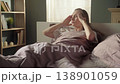 Young woman lying in bed suffering from a severe headache, massaging her temples with her fingers. Stressed and unwell person experiencing health problems and pain in the morning 138901059
