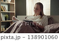 Peaceful young woman relaxing in her comfortable bed in the morning, enjoying a captivating book and turning pages in a cozy sunlit bedroom, representing a quiet lifestyle and hobby 138901060