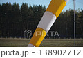 Tilt up shot of bright striped windsock, closeup. Analog wind vane of white and yellow colors stands on ground of airport showing weak wind. 138902712