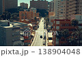 The camera shows a busy street filled with cars and buildings during the day. People walk along the sidewalks while the sun shines brightly. The city is lively and active. 138904048