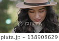 Portrait of a happy woman with dark curly hair and a wide smile, dressed in a trendy hat, enjoying a sunny day outside. The background is softly blurred, emphasizing her positive energy and fresh look 138908629