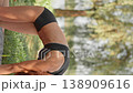 Red haired woman in black sportswear does yoga stretches on a mat in a lush green park, basking in sunlight. The serene outdoor setting highlights relaxation, fitness, and mindfulness in nature 138909616