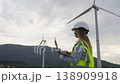 A woman engineer stands outdoors with a laptop, monitoring wind turbine performance at a wind farm. The scene highlights innovation, green energy, and the role of women in engineering fields 138909918