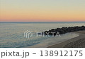 Calm shoreline with waves and rocky breakwater at sunset 138912175