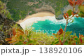 Foamy ocean waves roll onto sandy beach below steep tropical cliffs in Indonesia 138920106