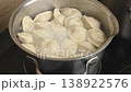 Many light-colored dumplings boil vigorously in a metal pot on a stovetop in a home kitchen. The water bubbles around them during preparation 138922576
