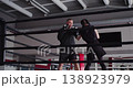 Watch a focused young Caucasian woman train with her boxing coach, striking the pads with precision and strength. Every punch showcases her commitment to mastering the art of boxing. 138923979