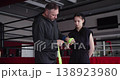 A trainer applies protective wraps to a young female boxer's hands before training, providing protection and support to her wrists and knuckles in preparation for intense boxing training. 138923980