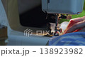 Focused hands guide blue fabric under the sewing machine's needle. The close-up captures the smooth stitching process and the skill required for perfect seams. 60 fps 4k footage. 138923982