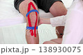 Physiotherapist applying kinesiotape to patient knee in clinic closeup 138930075