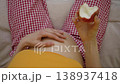 Expectant mother caressing her belly and eating healthy fruit, top view. Pregnant woman enjoying a fresh apple while relaxing in bed during a happy and quiet morning at home 138937418
