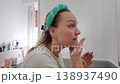 Determined to start the day fresh, a woman applies her skincare routine in a bright, cozy bathroom setting 138937490