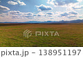 Low angle aerial flight over a vibrant green field towards a mountain range under a blue sky 138951197