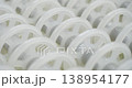 An industrial conveyor is in operation, white plastic rollers are rotating. Static handheld shot of production, sorting, or transportation line, real time speed, artificial lighting. 138954177