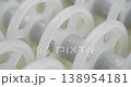 An industrial conveyor is in operation, white plastic rollers are rotating. Static handheld shot of production, sorting, or transportation line, real time speed, artificial lighting. 138954181