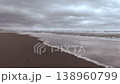 A cinematic wide shot of a powerful, turbulent ocean during a storm. Dark, heavy clouds hang over the horizon as large, foamy waves relentlessly roll onto the dark shore. The footage captures the raw  138960799