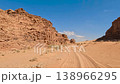 Aerial view of red sand dunes and sandstone mountains along a desert trail under a clear blue sky in 138966295