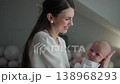 Mother holding newborn baby cradling infant gently with tender smile. Woman parent child family love joy parenthood cozy home adorable moment childhood innocence peaceful calm comfort. 138968293