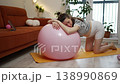 Expectant mother feeling tired during her prenatal fitness routine, resting her head on a large pink stability ball while kneeling on a yoga mat in her cozy living room 138990869