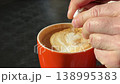 Cappuccino in orange cup sunlight male hands adding sugar stirring coffee closeup cafe drink 138995383