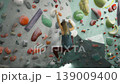 slender girl climber in sports outfit is climbing up colorful artificial wall in gym gripping rocks focused of extreme activity. Youth, entertainment and training concept. dynamic motions 139009400