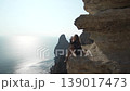 Traveler, cliff, sea. Young woman sitting on a high rock enjoying ocean view and feeling freedom during summer vacation. 139017473