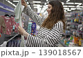 Young pregnant woman joyfully browsing the baby section of a large supermarket, carefully selecting adorable bodysuits and clothing for her future newborn while preparing for motherhood 139018567