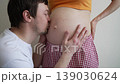 Young expectant parents sharing a tender moment as the husband touches, kisses, and listens to his wife's pregnant belly, anticipating their baby's arrival with love and happiness 139030624
