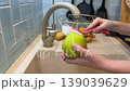 A vegan child practices kitchen hygiene, diligently brushing garden-fresh apples under running water in a sunny, domestic setting. 139039629
