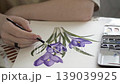 Artist painting purple iris flowers with watercolor on paper, close-up of hands. 139039925
