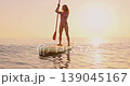 Happy young woman walking on stand up paddle sup board by the sea during summer vacation. Beautiful girl flat water paddling against sea and sky background. Healthy lifestyle concept. Slow motion 139045167