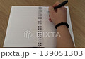 A hand writing notes in a spiral notebook on a wooden table. 139051303
