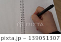 Close-up of a hand writing in a grid notebook. 139051307