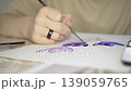Close-up of a teenage student's hand painting purple flowers with watercolor. 139059765