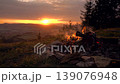 A blazing bonfire atop a mountain in the Karkonosze range, overlooking the setting sun during the golden hour, with Sniezka peak visible in the background. 139076948