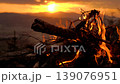A blazing bonfire atop a mountain in the Karkonosze range, overlooking the setting sun during the golden hour, with Sniezka peak visible in the background. 139076951