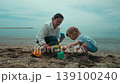 Mother and son share joyful moments playing together by the sea, building sandcastles and high-fiving. A perfect summer day for family fun and memories. 139100240
