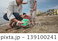 A heartwarming scene of a mother and her young child enjoying a sunny day at the beach in Malaga. They happily play with sand and a green bucket, creating joyful family memories. 139100241