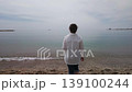 A serene moment captured as a woman in a white shirt and jeans walks barefoot into the tranquil waters of Malaga beach. She finds peace and relaxation by the sea on a quiet, contemplative day. 139100244