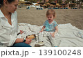 A mother and her young child share a delightful beach picnic in Malaga, creating beautiful memories under the warm Mediterranean sun. 139100248