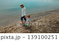 A serene moment of a mother and her young child walking hand-in-hand along the peaceful shoreline, enjoying the calm sea and sandy beach. 139100251