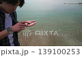 A curious young man on a beach discovers and gently holds a small crab, showcasing a moment of connection with marine life and nature by the sea. 139100253